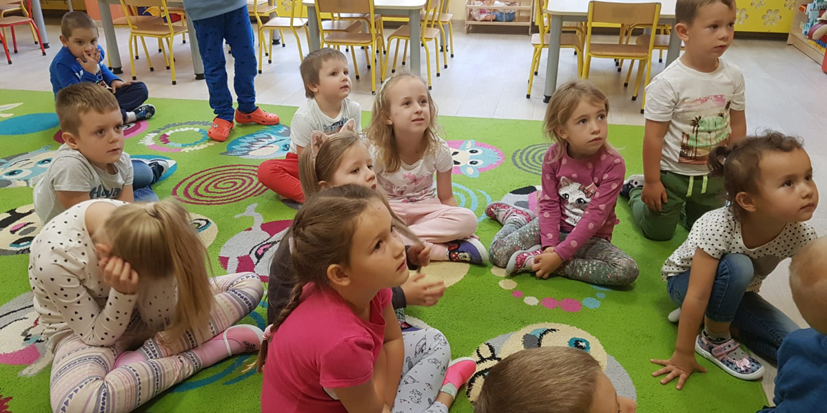 dzieci siedzą na dywanie i słuchają bajki o „Tupciu Chrupciu” czytanej przez panią
