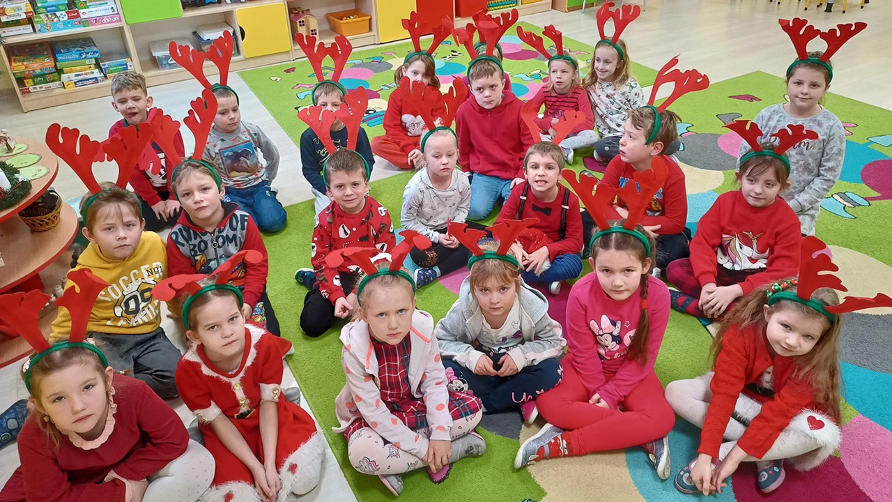 grupa dzieci ubrana na czerwono prezentuje buciki od Św. Mikołaja