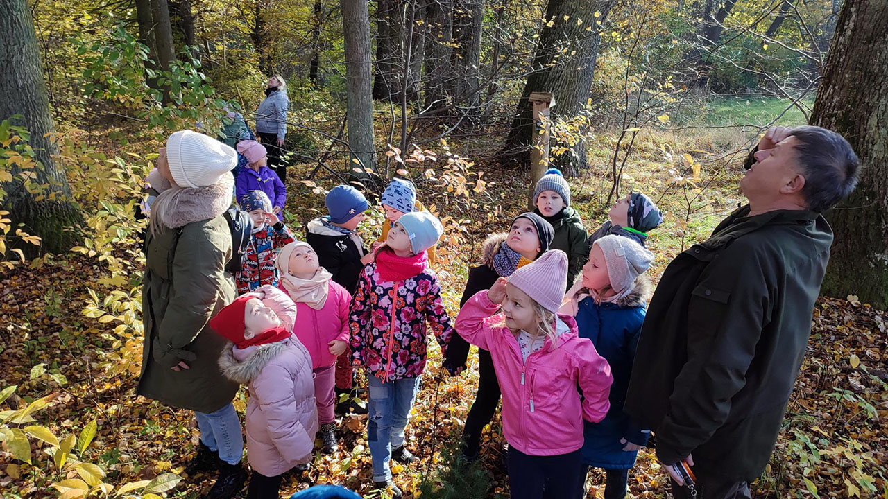 Dzieci słuchają ciekawostek przekazywanych przez leśniczego.